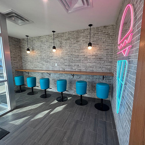 interior of the burger parlour, a restaurant in sylvan lake, with brick walls, blue stools at a counter, and a neon sign in the shape of an ice cream cone