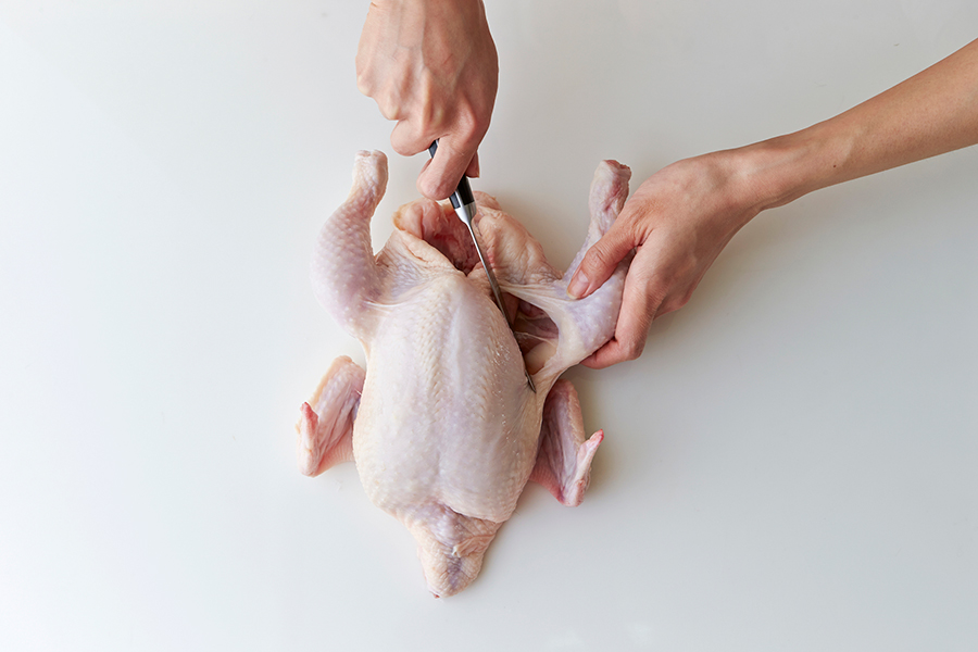 male hands butchering a whole raw chicken