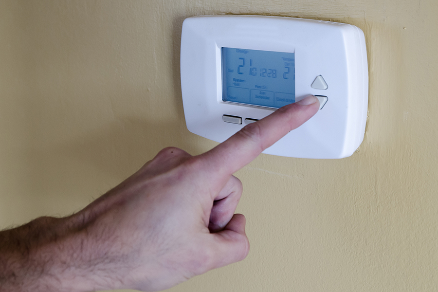 man's hand lower temperature on thermostat