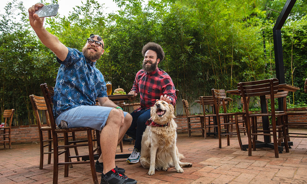 two friends taking a photo of themselves with a dog on a restaurant patio