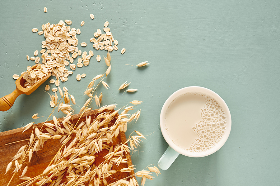 mug of oat milk with oat flakes and raw grain on a blue background
