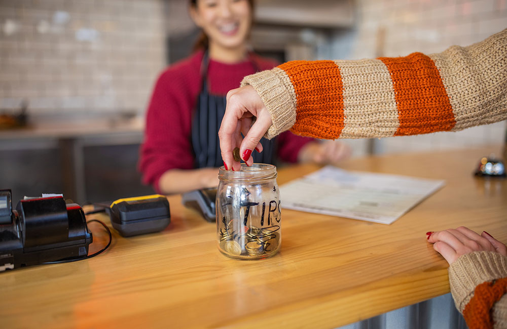 person dropping money into tip jar at cafe
