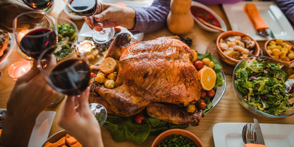 people raising wine glasses over a roasted turkey in the middle of the table